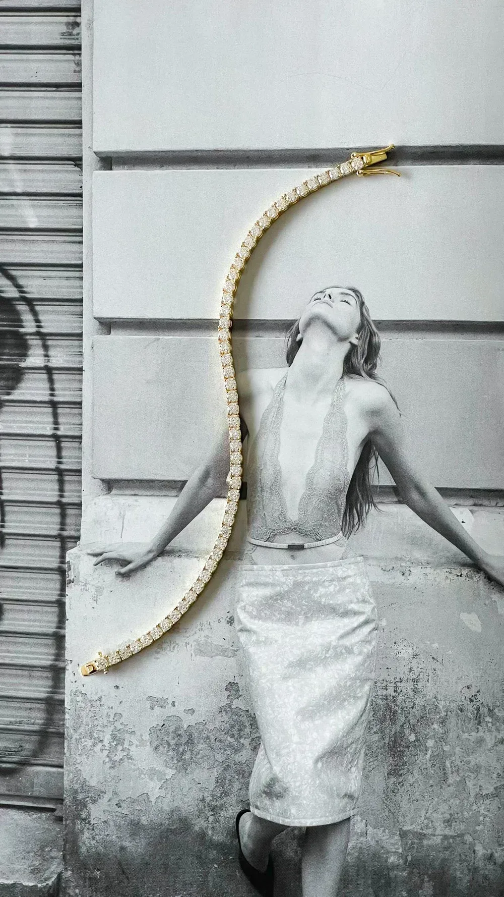 A yellow gold diamond tennis necklace against a black-and-white editorial portrait