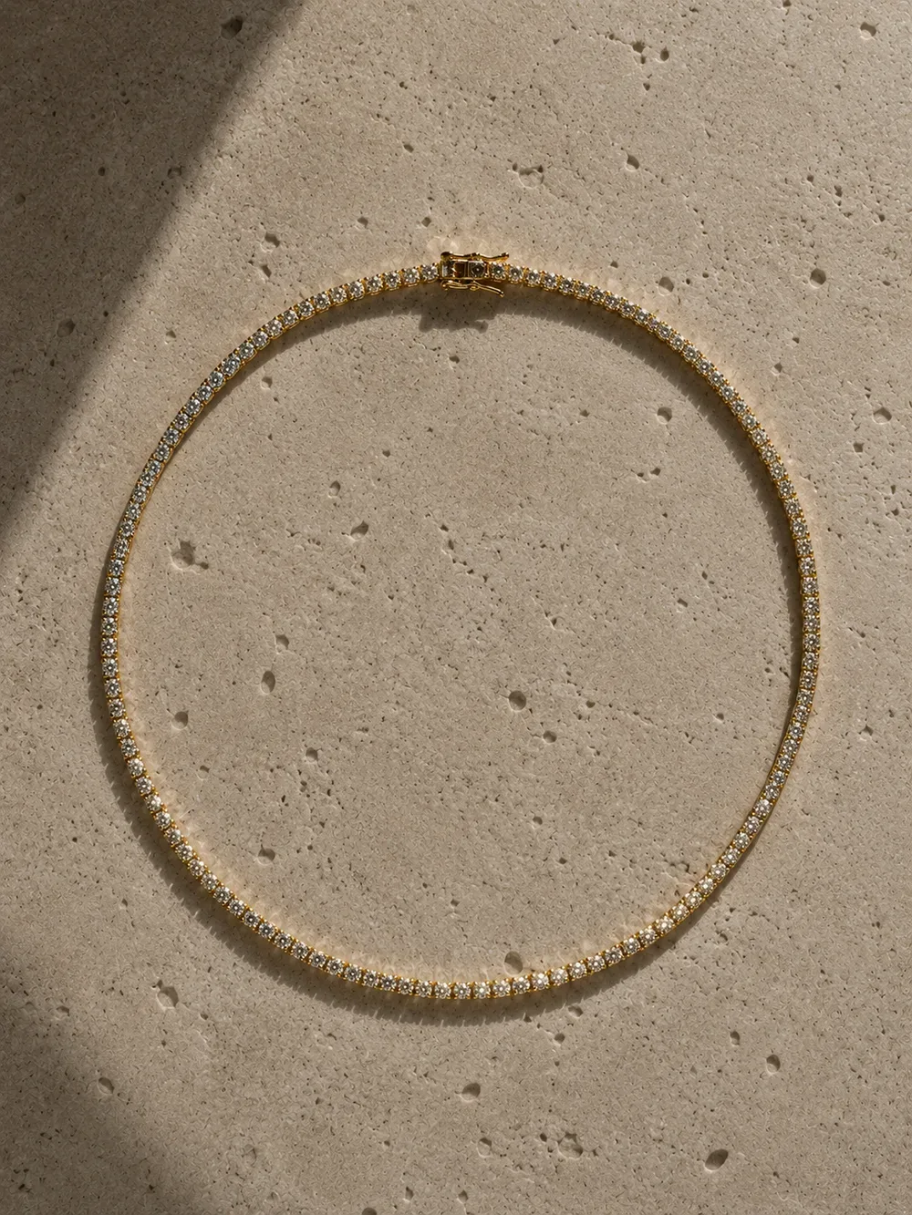 A yellow gold diamond tennis necklace coiled into a circle on limestone