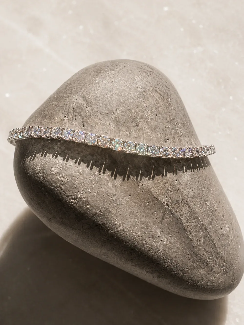 A white gold diamond tennis bracelet resting over a smooth grey stone